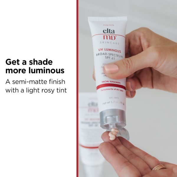 Large text “Get a shade more luminous” over smaller text “A semi-matte finish with a light rosy tint” to the left of EltaMD UV Luminous SPF 41 tinted sunscreen product being squeezed onto fingers